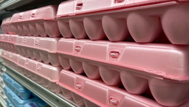 Pink egg cartons stacked on a shelf in a grocery store.