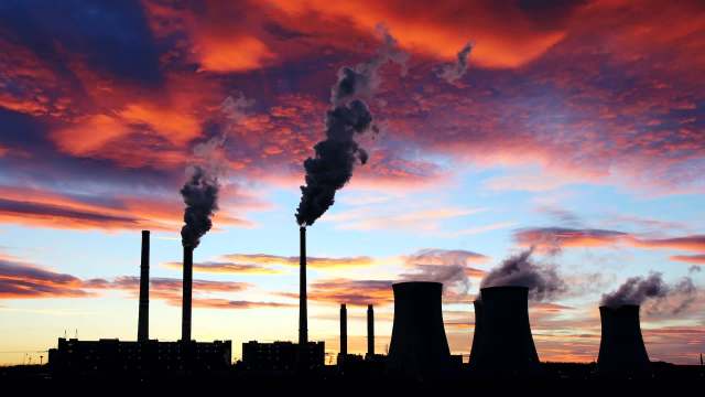 Industrial smokestacks emit smoke against a colorful sunset sky.