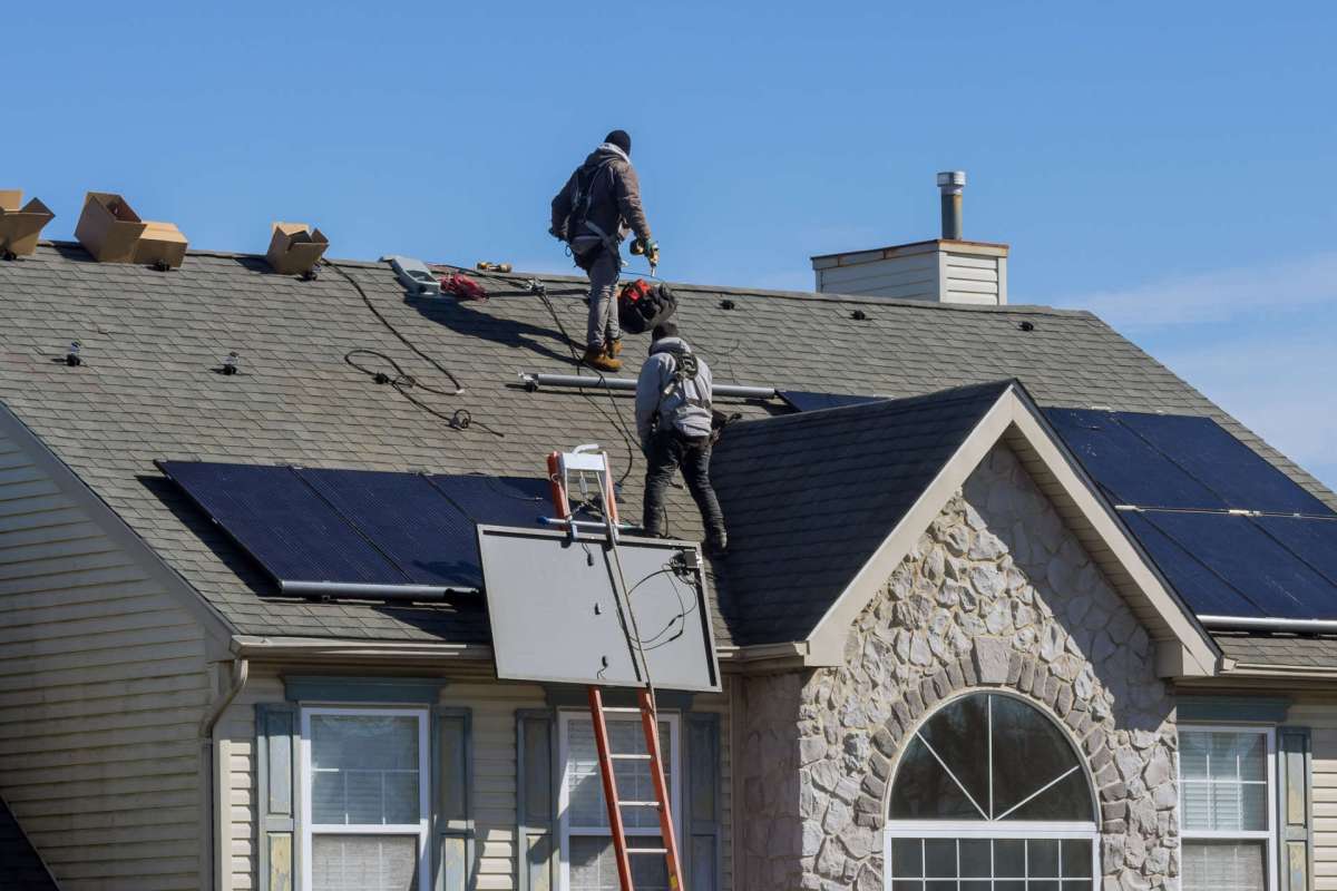 Two workers install solar panels on a pitched roof.