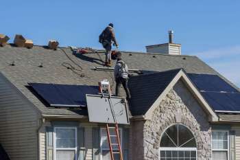 Two workers install solar panels on a pitched roof.