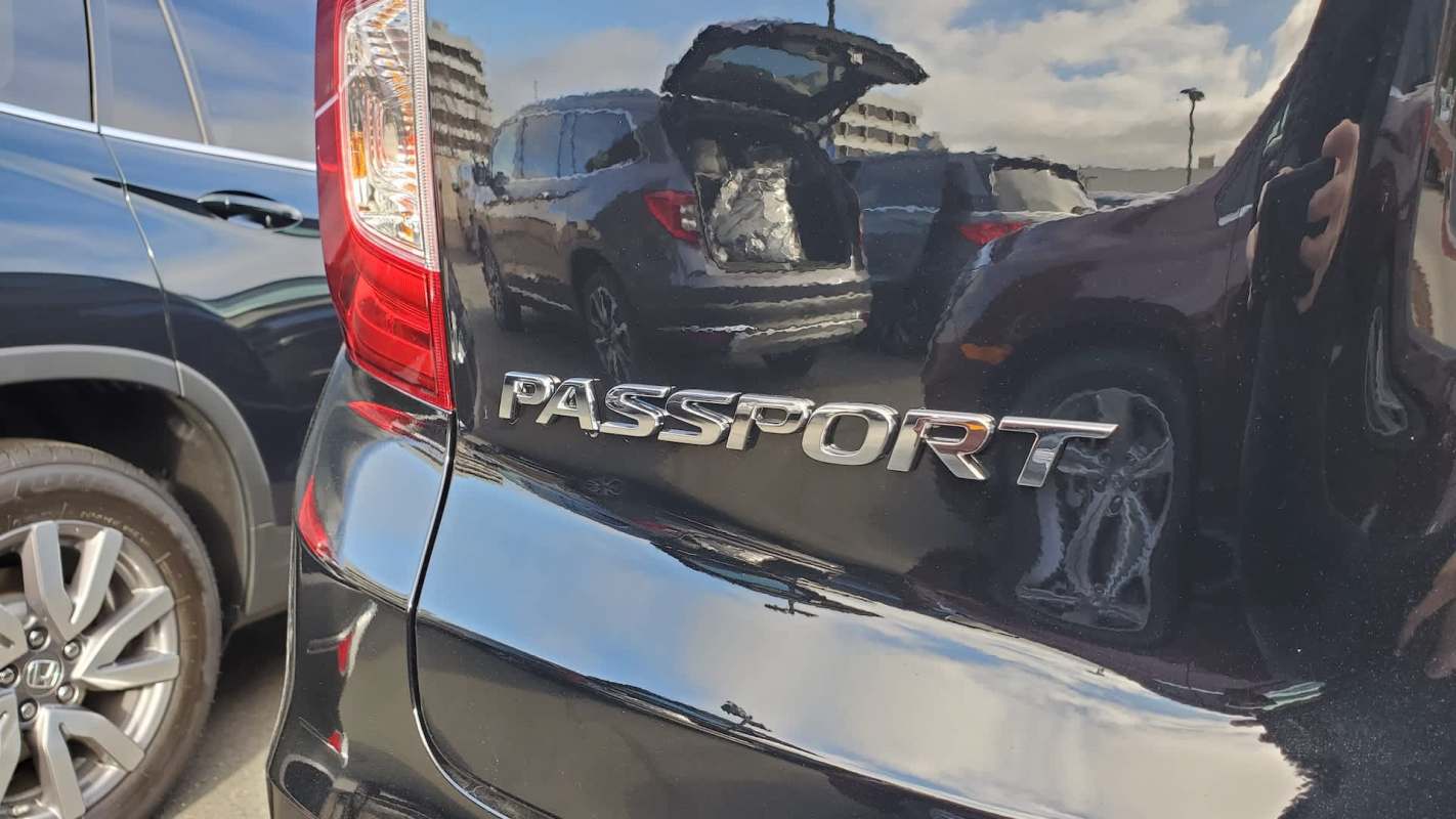 The rear of a black SUV displaying the "PASSPORT" emblem with reflections of other vehicles in the background.