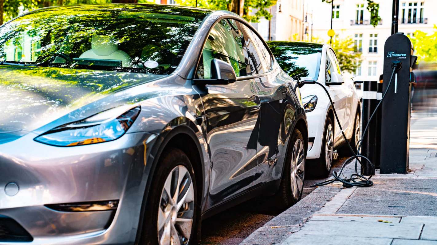 Two electric vehicles parked and charging at a public charging station on a city street.