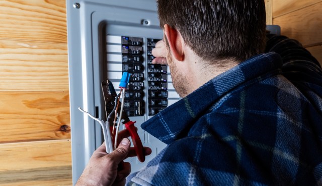 A person working on a circuit breaker panel with electrical tools in hand.