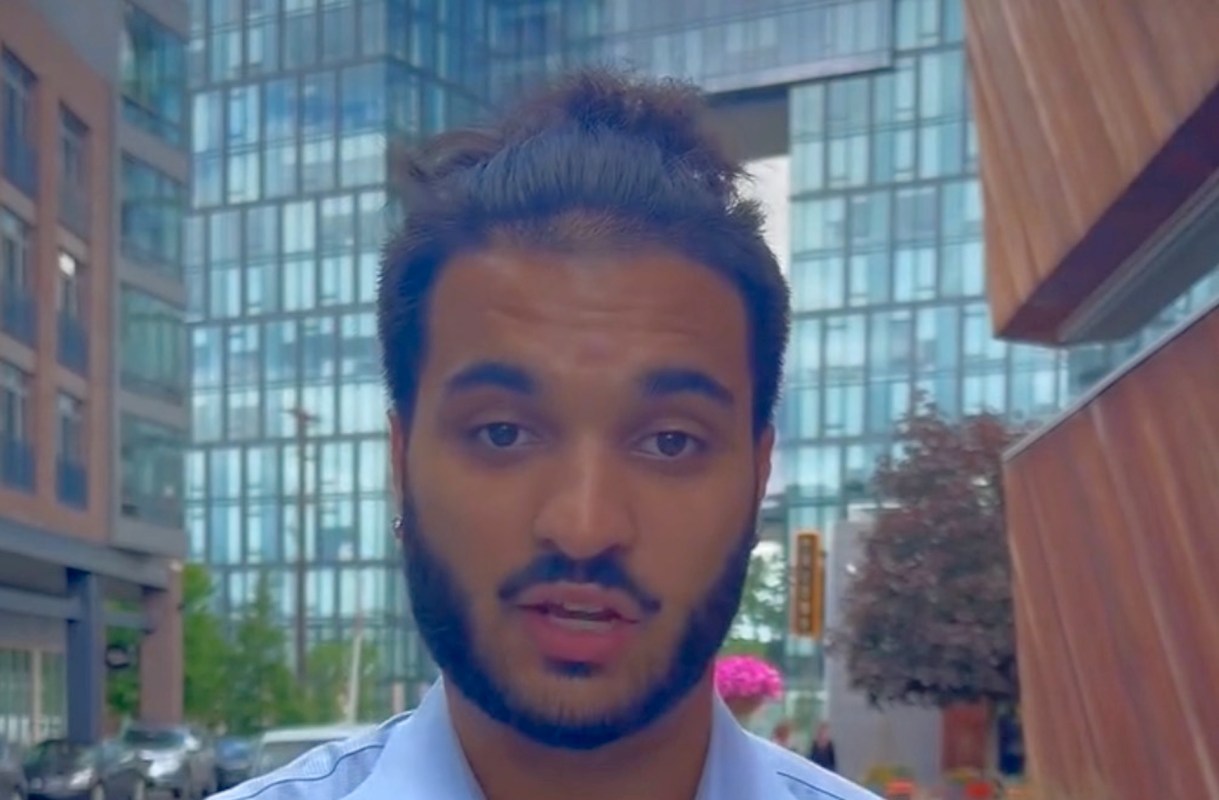 A man stands on a city street with modern buildings in the background.