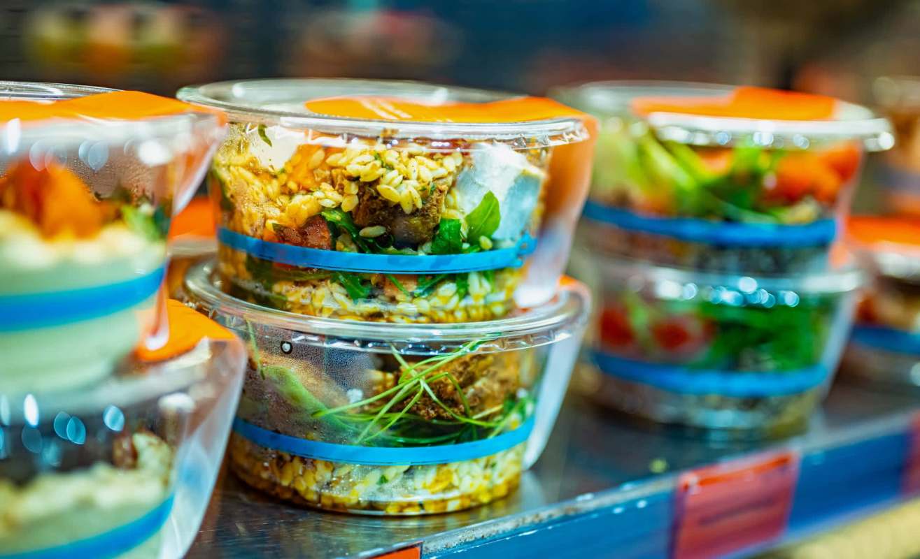 Containers of assorted salads are stacked on a shelf, featuring various ingredients and colorful toppings.