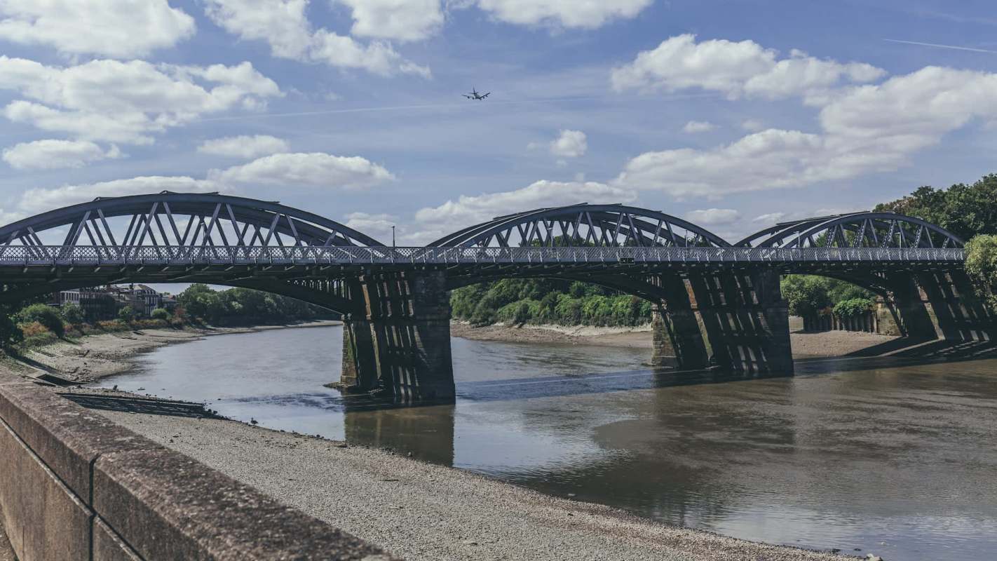 A metal arch bridge spans a river under a cloudy sky.