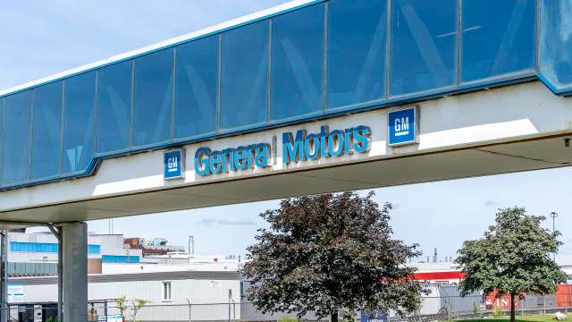 A "General Motors" sign on a walkway above an industrial area with trees.