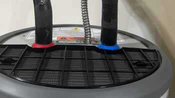 A close-up of a machine with two colored hoses and a grid surface displaying warning labels.