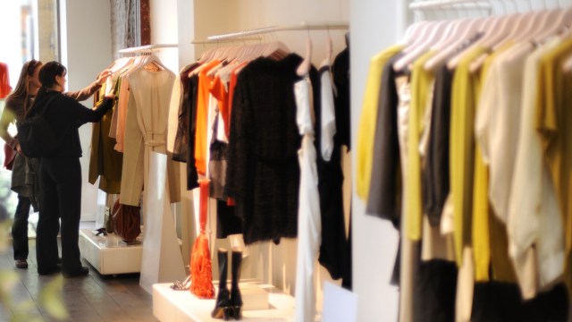 A woman browsing clothing on display racks in a retail store.