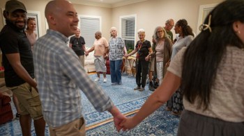 People holding hands in a circle in a community room.