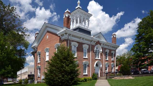 Manchester, Tennessee, courthouse with white trim, surrounded by trees and a grassy area, under a blue sky with clouds.