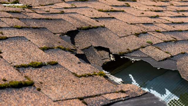 Damaged roof shingles with moss growth and a visible hole exposing an interior area.