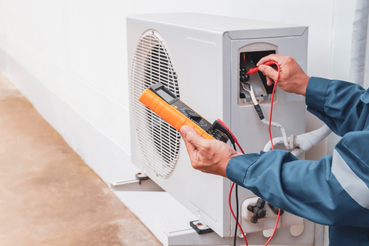 A technician uses a multimeter to test an outdoor air conditioning unit.