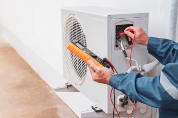 A technician uses a multimeter to test an outdoor air conditioning unit.