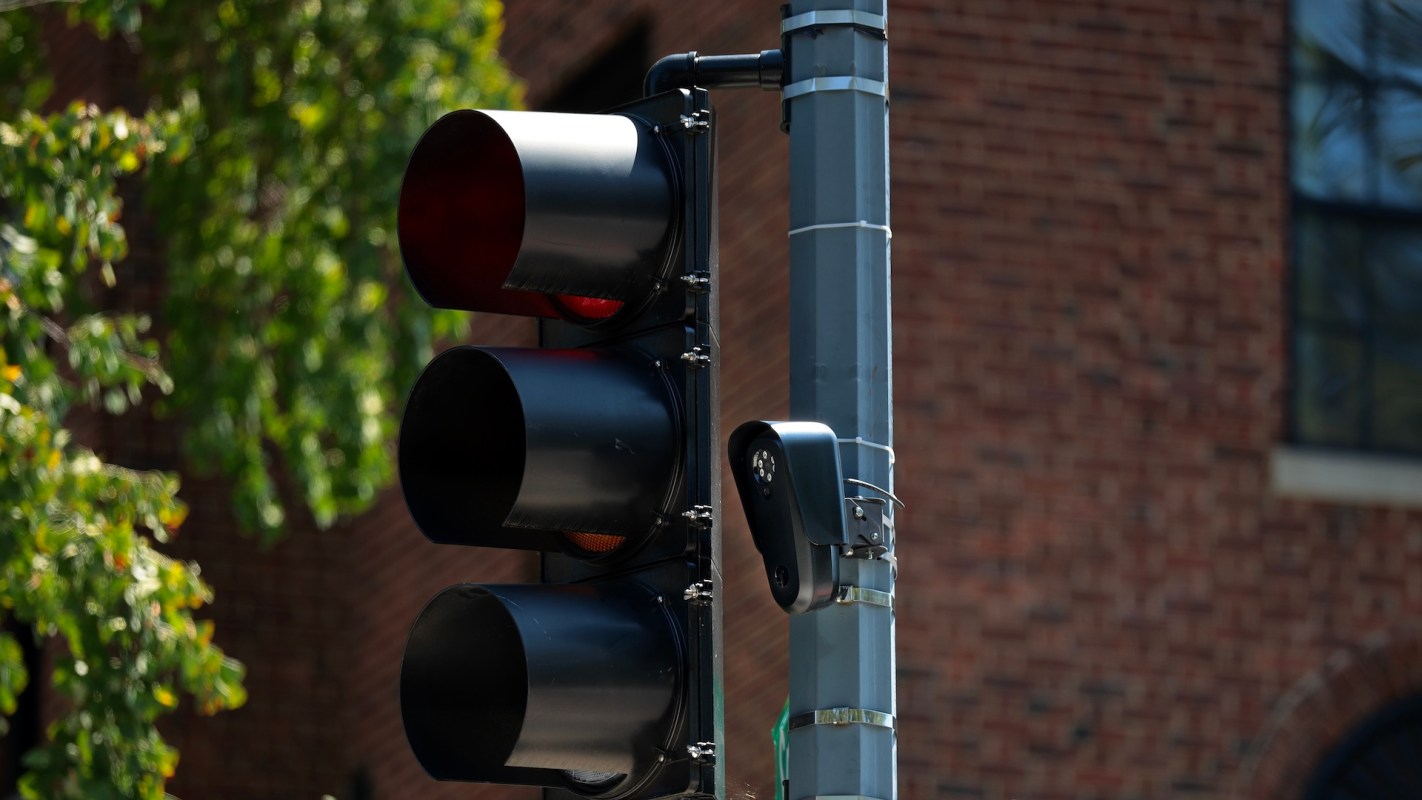 A traffic light displaying red signals mounted on a pole beside a brick wall.
