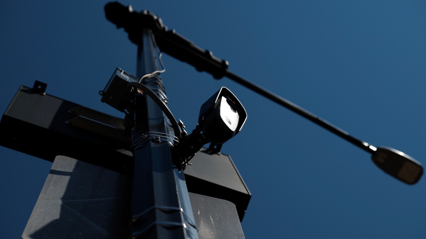 A streetlight and surveillance camera mounted on a pole against a clear blue sky.