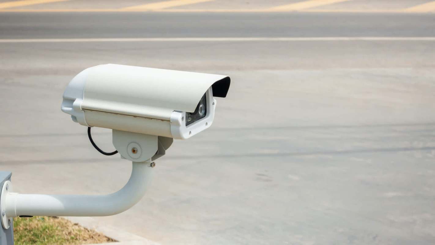 A security camera is mounted on a support, facing a road.