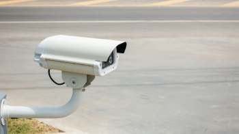 A security camera is mounted on a support, facing a road.