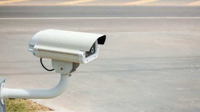 A security camera is mounted on a support, facing a road.