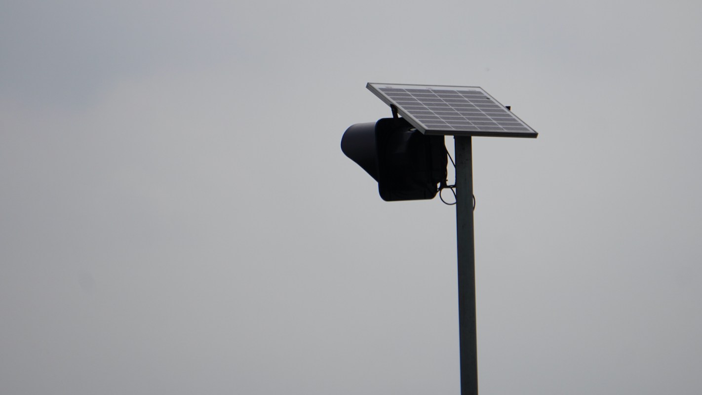 A Flock safety camera mounted on a pole against a cloudy sky.