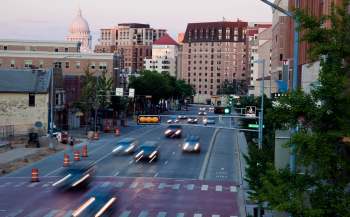 A street view of Madison, Wisconsin, featuring traffic lights and vehicles in motion.