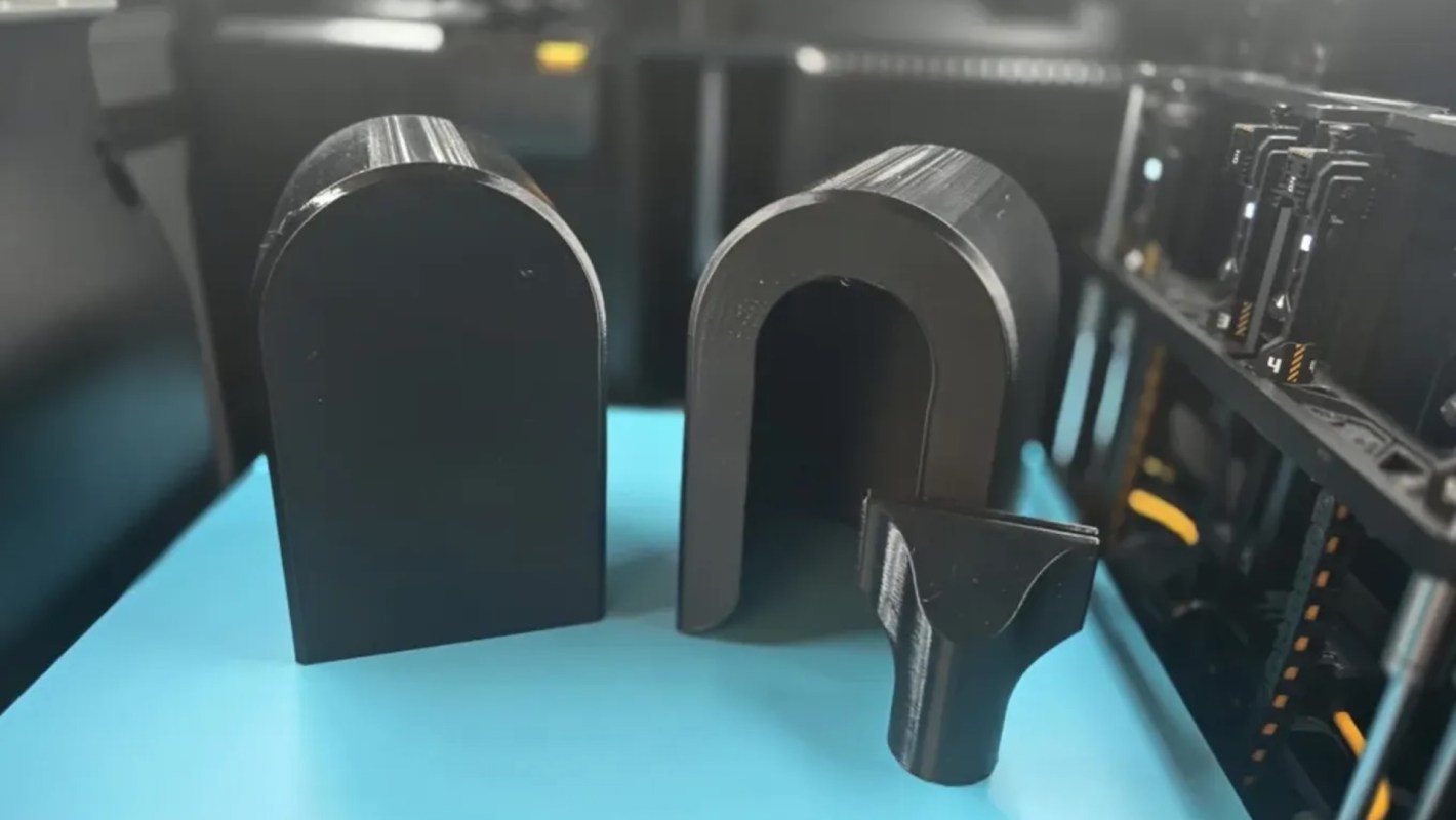Three black 3D-printed shapes, including two arch-like forms and a smaller angled piece, on a blue surface.
