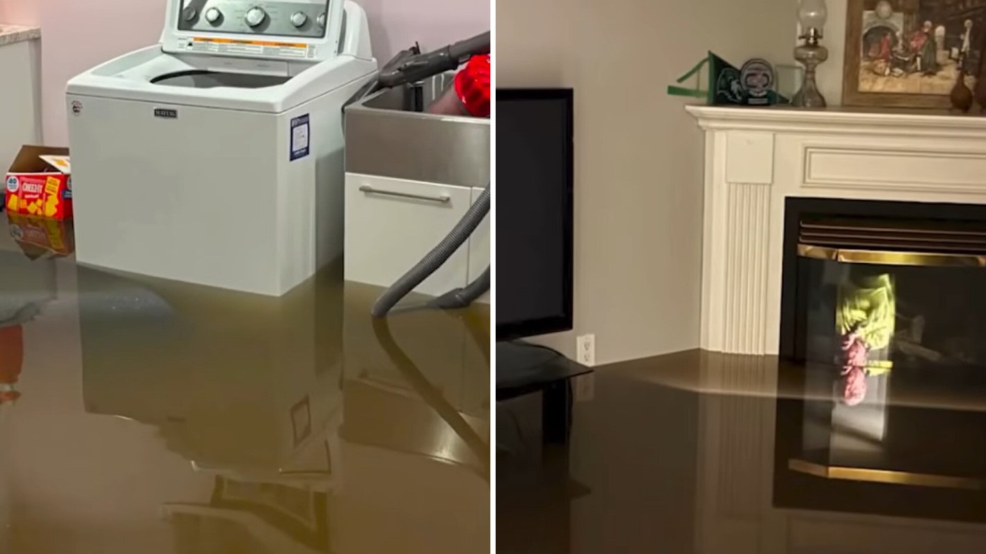 A flooded living space with water surrounding a washing machine and reflecting a fireplace.