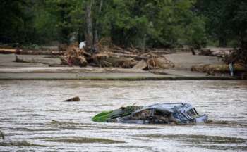 A submerged car in a river with debris and trees in the background.