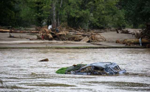 A submerged car in a river with debris and trees in the background.