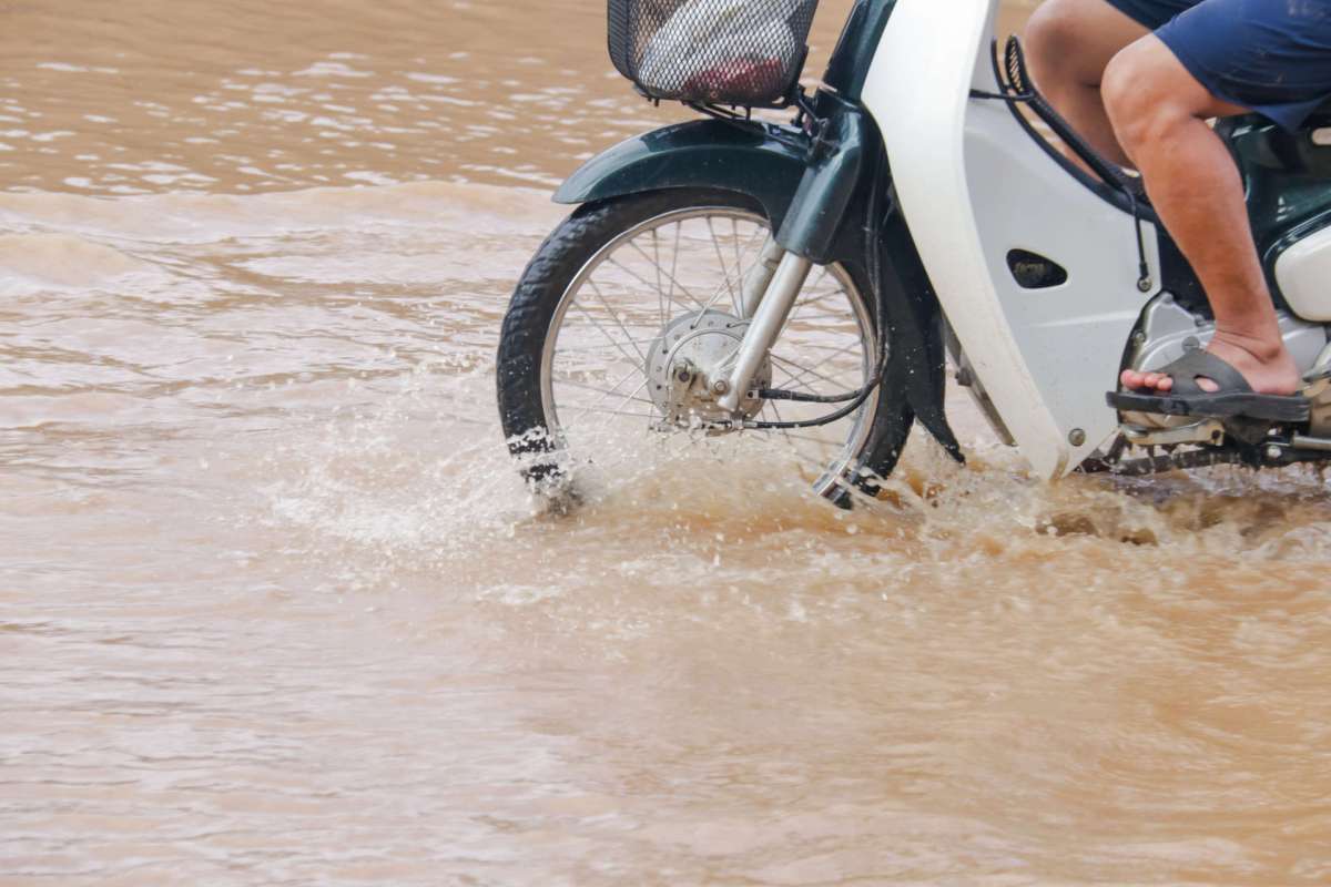 A motorbike rides through a flooded area, creating splashes of water.