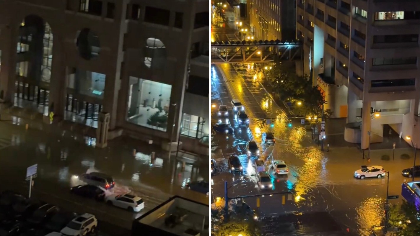 A flooded urban street at night with several cars navigating the water.