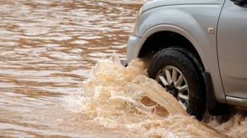 A vehicle drives through a flooded area, causing water to splash around the tires.