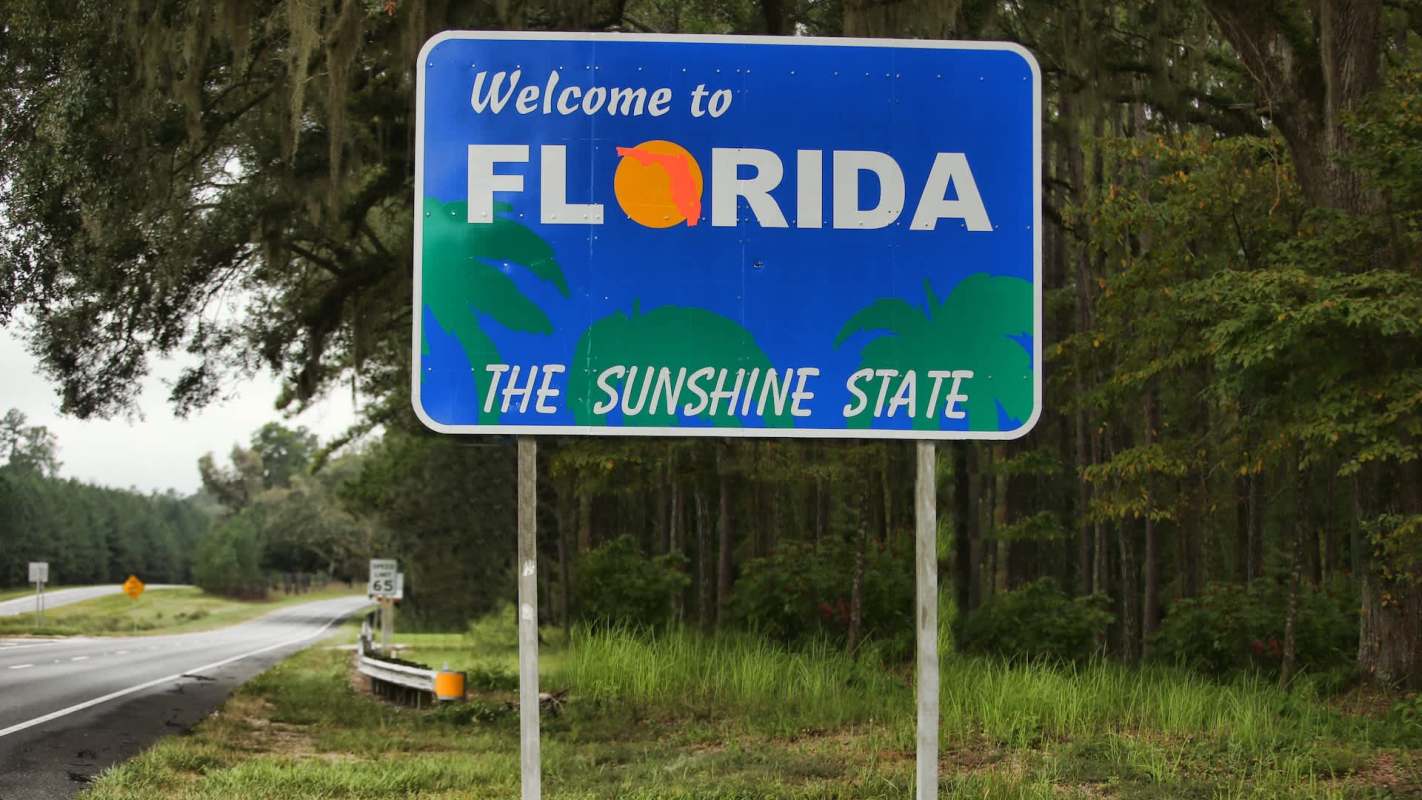 A welcome sign for Florida, featuring palm trees and the phrase "The Sunshine State."