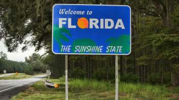 A welcome sign for Florida, featuring palm trees and the phrase "The Sunshine State."