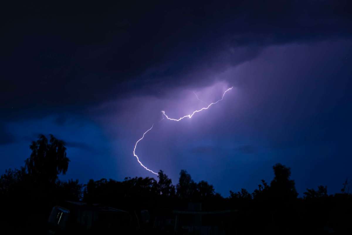 Lightning strikes through dark, stormy clouds illuminated by a blue sky.