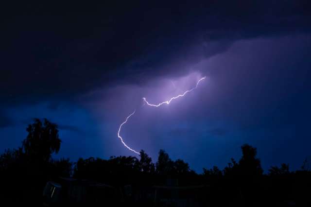 Lightning strikes through dark, stormy clouds illuminated by a blue sky.