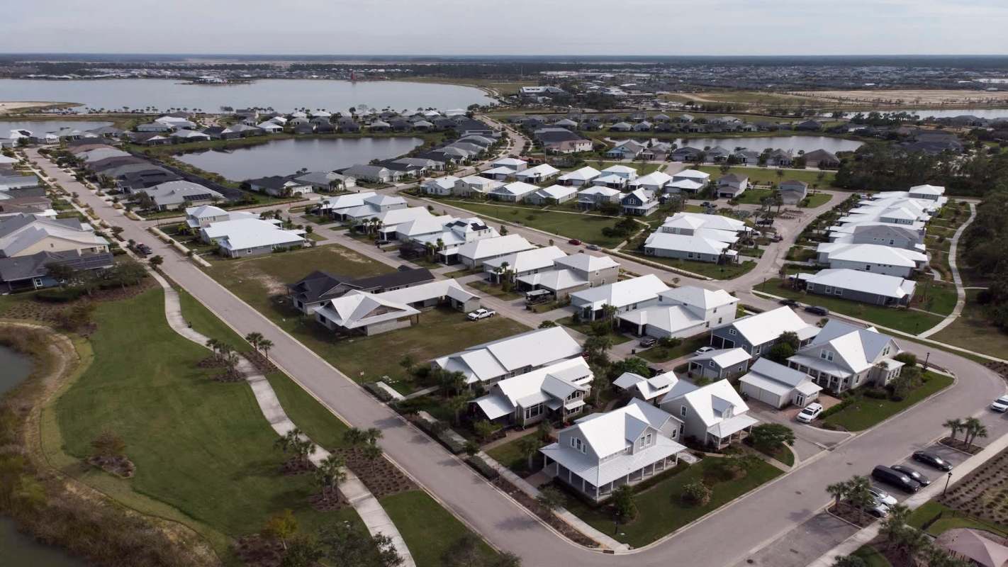 Aerial view of a suburban area with houses, roads, and nearby bodies of water.