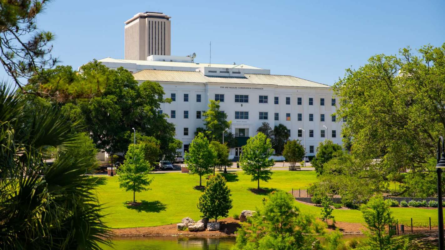 A government building surrounded by green trees and grass near a small pond.