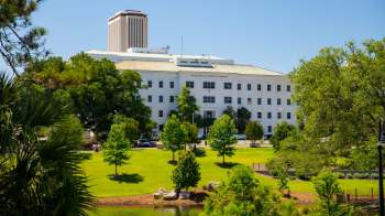 A government building surrounded by green trees and grass near a small pond.