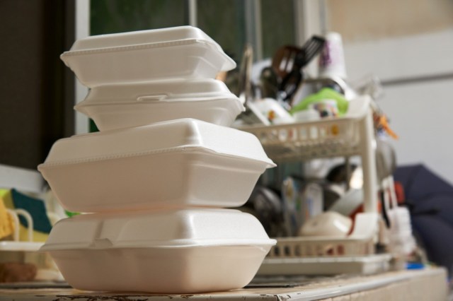 Stacked takeout containers on a table with a dish rack in the background.