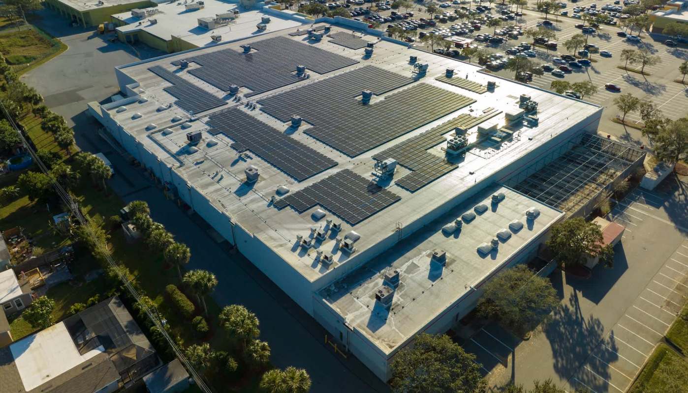 A large building rooftop covered with solar panels and HVAC units, adjacent to a parking lot.
