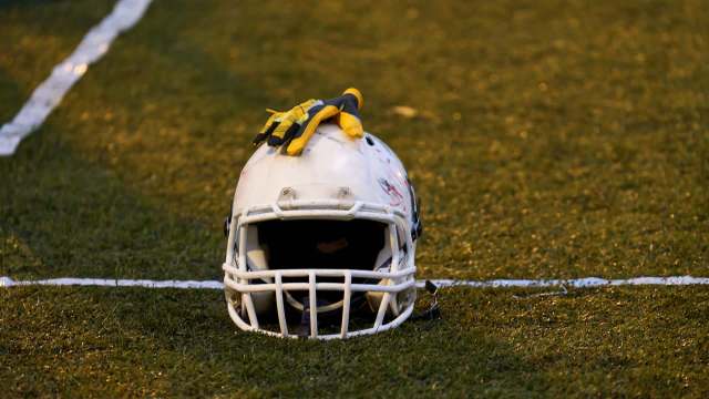 A football helmet with gloves resting on top is placed on a grassy field.