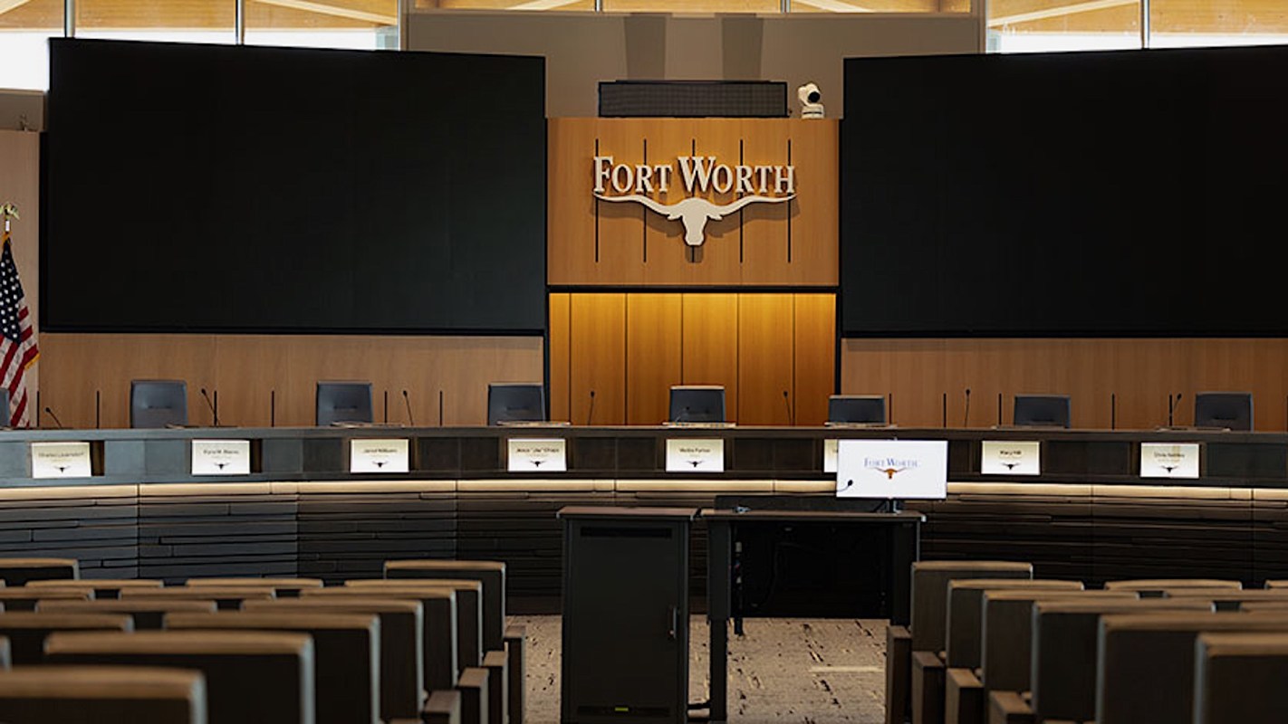 A conference room with a long table, chairs, and a large screen displaying "Fort Worth."