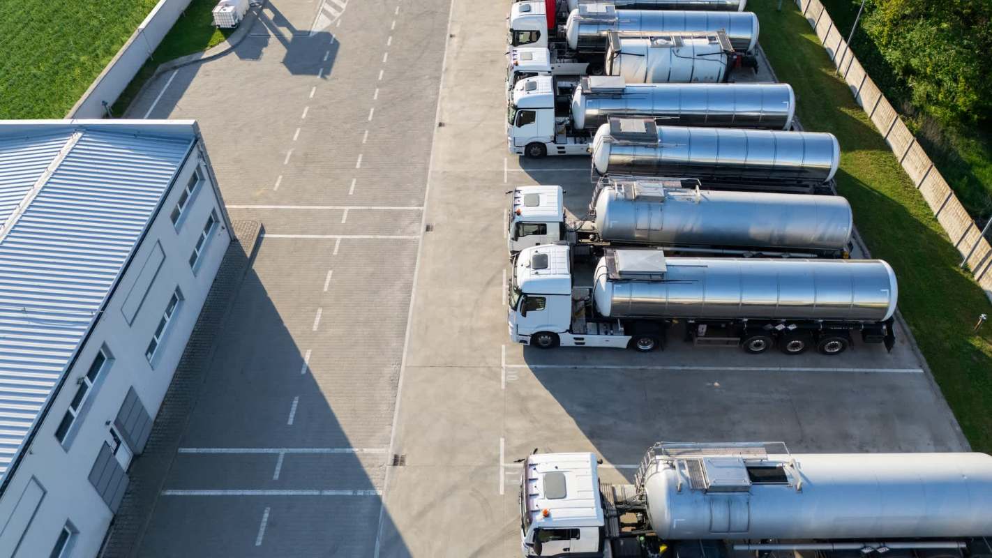 Multiple tanker trucks parked in a lot next to a building and green space.