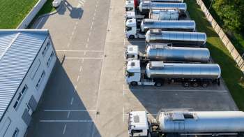 Multiple tanker trucks parked in a lot next to a building and green space.
