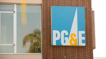 A sign for PG&E on a brick wall with reflections of a palm tree in the glass.