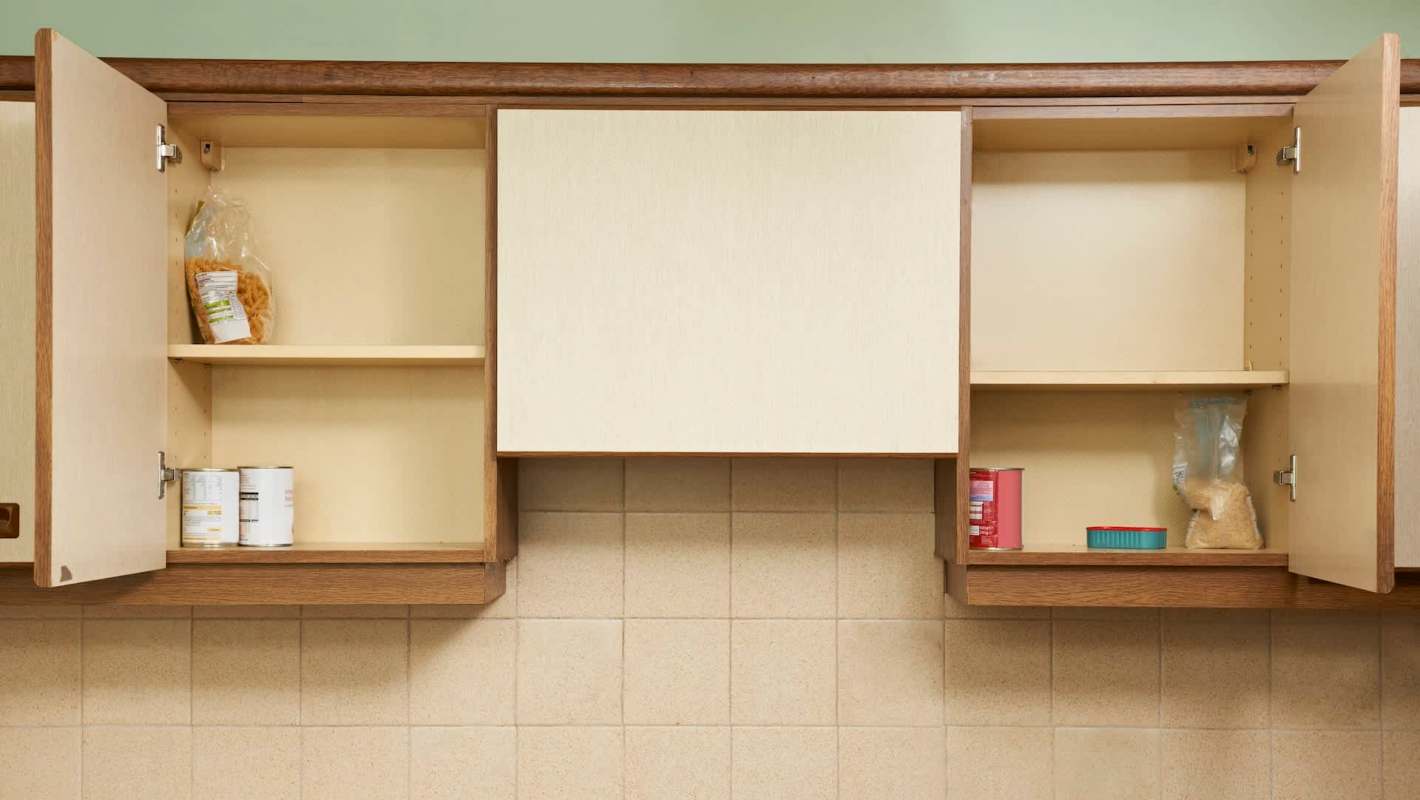 A kitchen cabinet with one open door, containing a few food items and empty shelves.