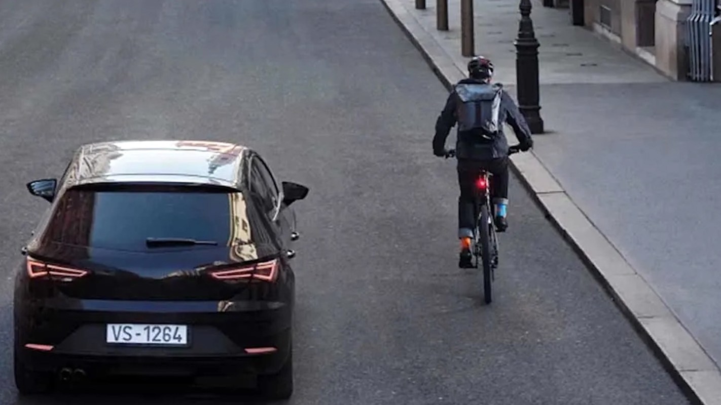 A cyclist rides on a street alongside a parked black car.