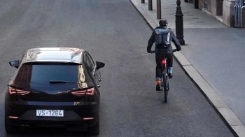 A cyclist rides on a street alongside a parked black car.