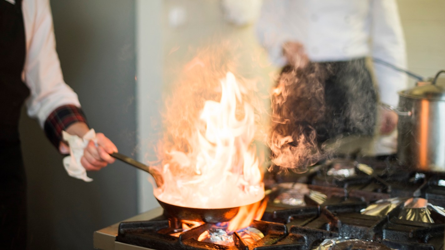 A flaming pan on a gas stovetop.